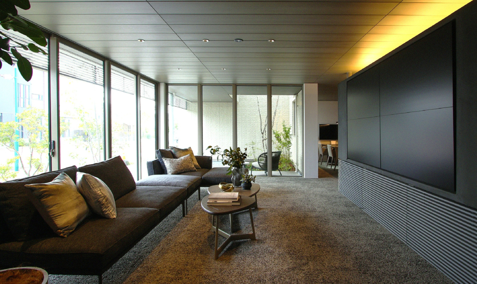 ダイナミックな開口部と、重厚感のあるインテリアが調和する１階。浮造り天井材と上質なカーペットに、洗練された家具を組み合わせて贅沢な空間に。「life knit atelier」は、お客様の感性を見つけ、その感性にお応えし、家という形にしていくための場所です。