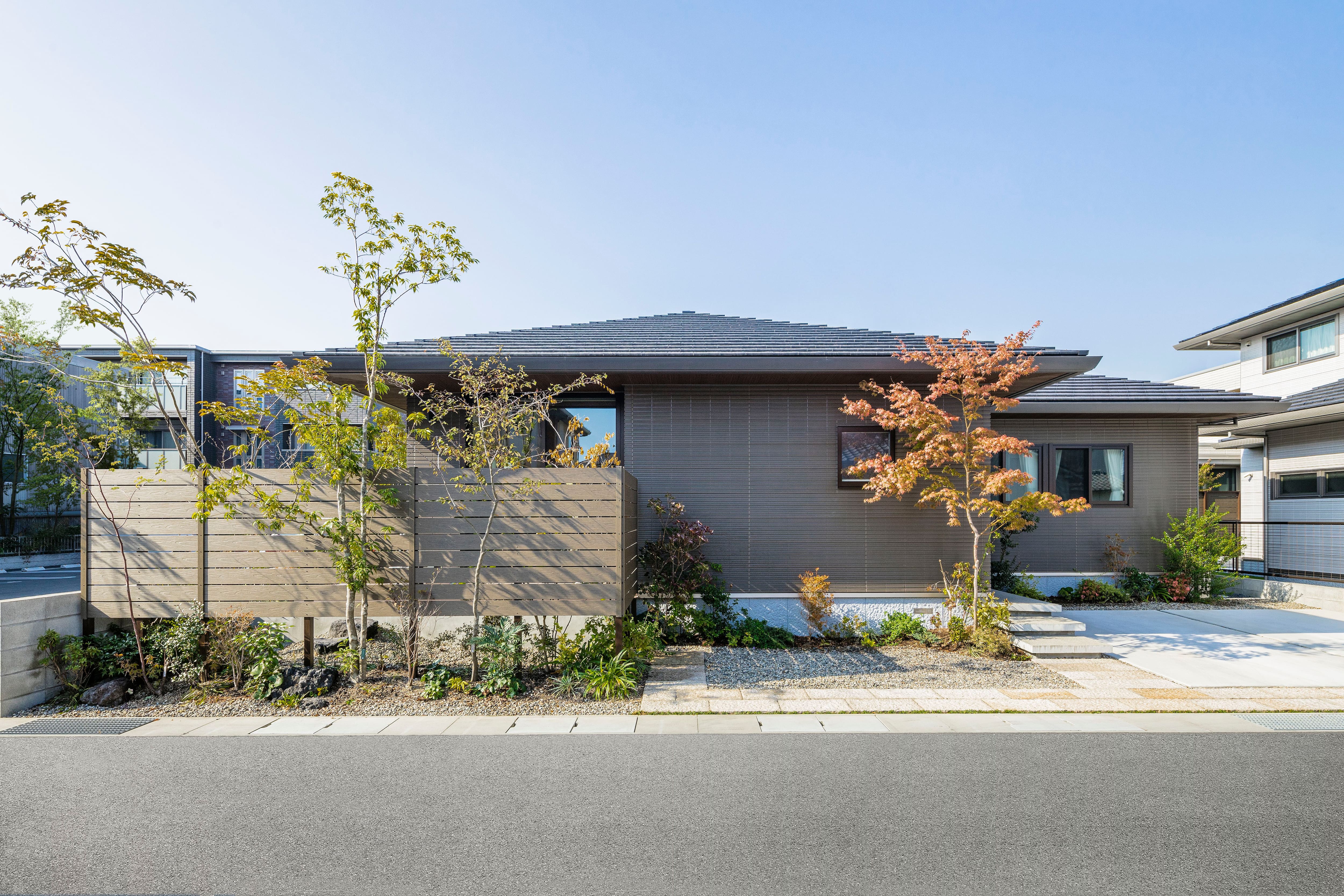 寄棟屋根と、濃色の陶板外壁ベルバーンを組み合わせたシンプルな外観。庭やアプローチに配した植栽が、より街並みに映える